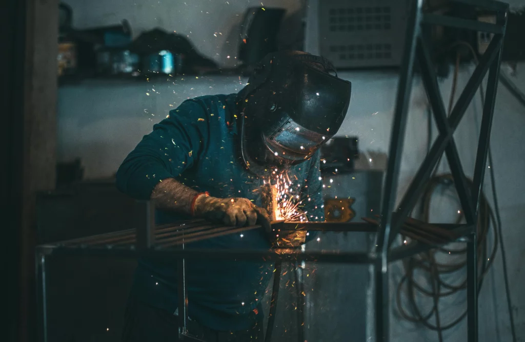 Metalworker welding steel frame in an industrial workshop wearing protective helmet and gloves